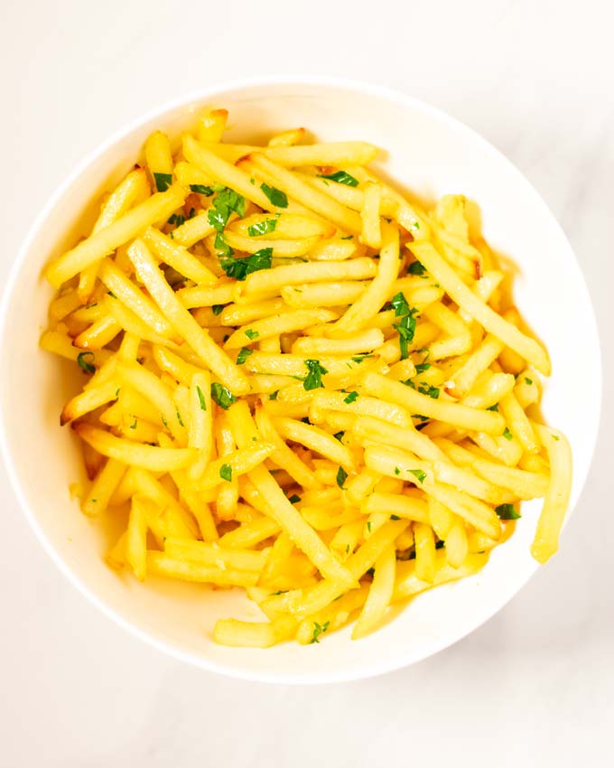 Top view on a white bowl with Garlic Fries garnished with parsley.