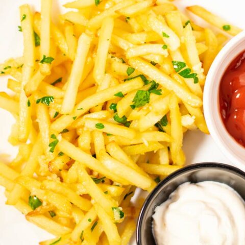 Top view on a portion of Garlic Fries, served with ketchup and mayo.