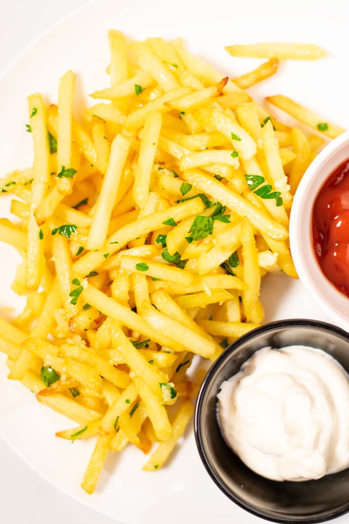 Top view on a portion of Garlic Fries, served with ketchup and mayo.