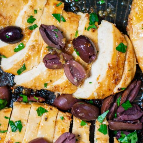 Closeup of sliced open Green Chicken breasts in a pan, garnished with olives and parsley.