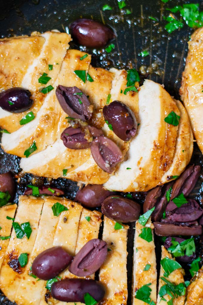 Closeup of sliced open Green Chicken breasts in a pan, garnished with olives and parsley.