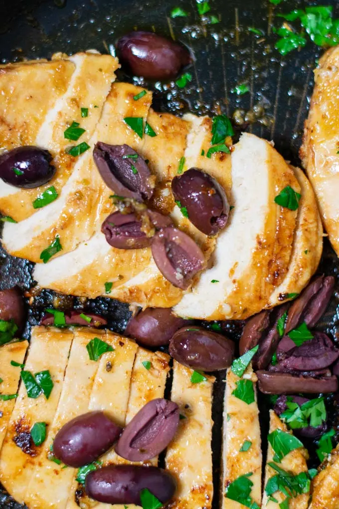 Closeup of sliced open Green Chicken breasts in a pan, garnished with olives and parsley.