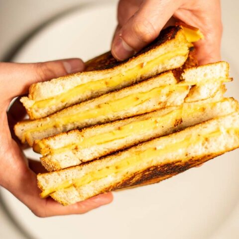 Four open Grilled Cheese Sandwiches are held in hands.