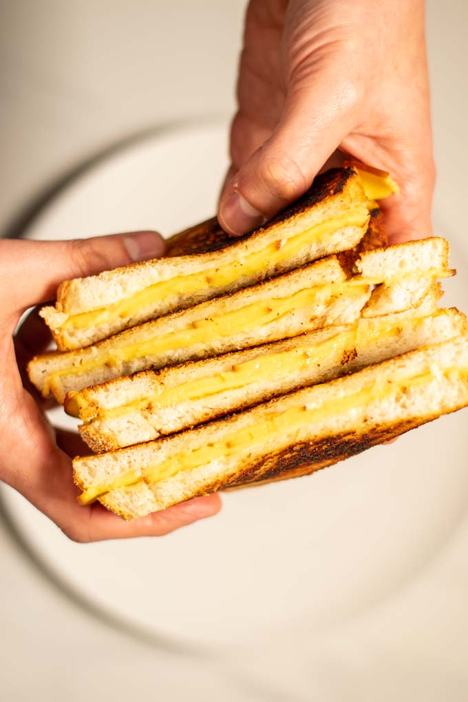 Four open Grilled Cheese Sandwiches are held in hands.