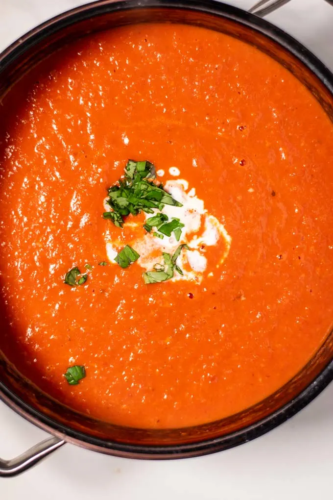 Closeup on the pot with the ready Tomato Soup, garnished with vegan cream and fresh basil.