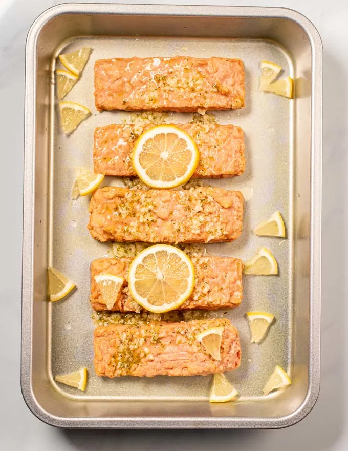 Salmon filets in a baking dish, marinated and garnished with lemon.