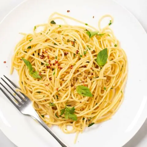 Top view on a portion of Garlic Pasta served on a white plate, with a silver fork.