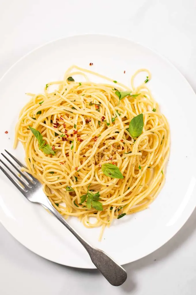 Top view on a portion of Garlic Pasta served on a white plate, with a silver fork.