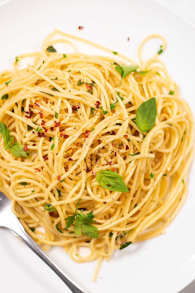 Closeup of a portion of Garlic Pasta, garnished with fresh basil and parsley, some chili flakes and black pepper.