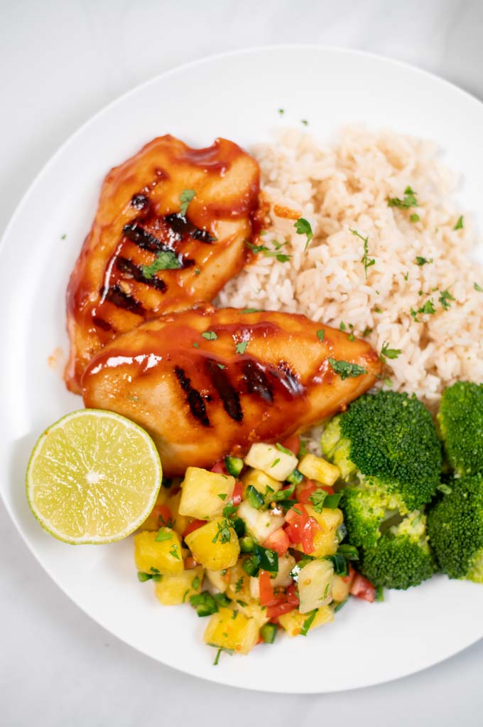 Portion of a Huli Huli Chicken in a plate, served with rice, broccoli and a pineapple salsa.