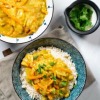 Two bowls with Japanese Curry: one served over white rice, the other plain. Some cilantro in the background.