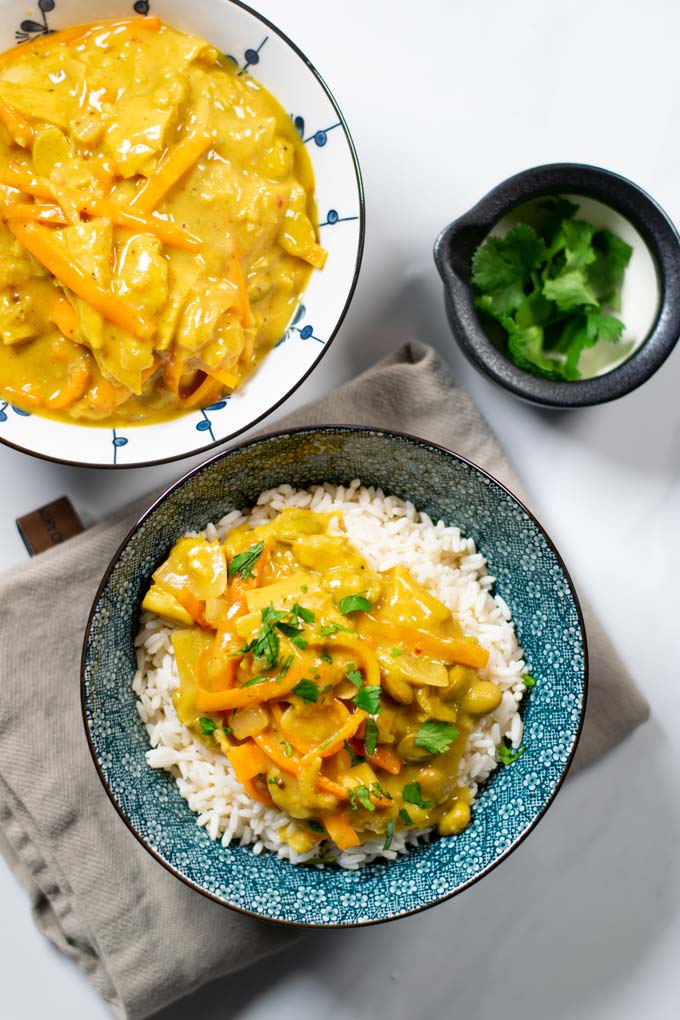 Two bowls with Japanese Curry: one served over white rice, the other plain. Some cilantro in the background.