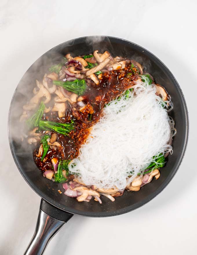 Top view of a large frying pan with broccoli, shiitake mushrooms, glass noodles, and stir Fry sauce.