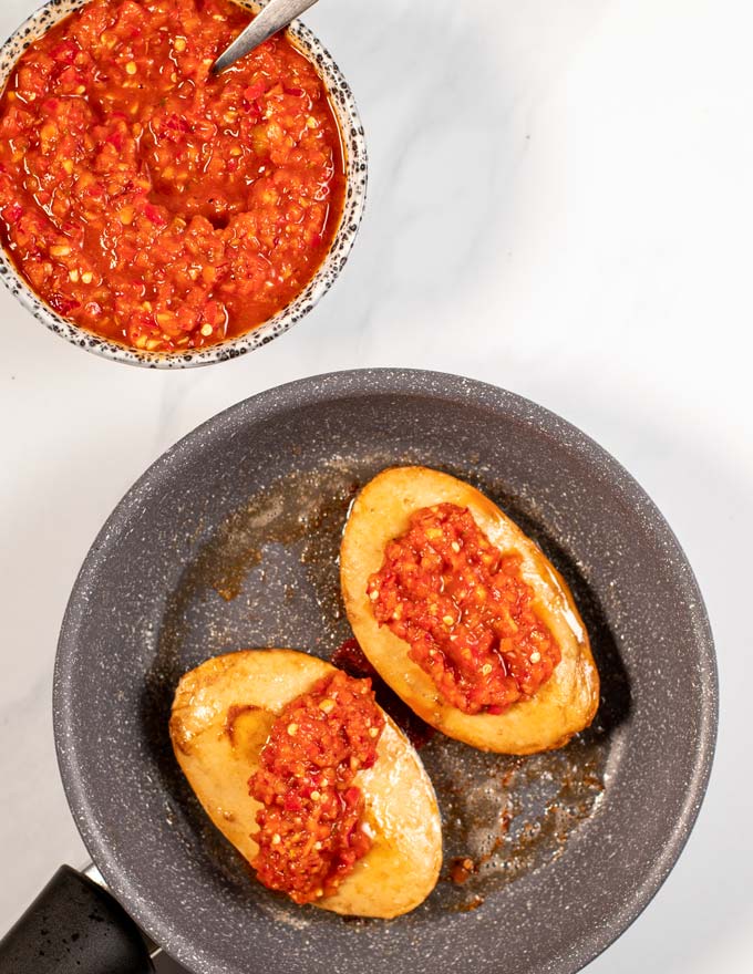 Two Peri Peri Chicken filets in a frying pan with a small serving bowl with the sauce in the background.