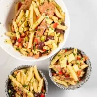 Two portions of Antipasto Salad are served in small bowls, the big serving bowl is in the background.