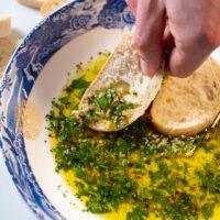 Bread dipped in oil is held by a hand.