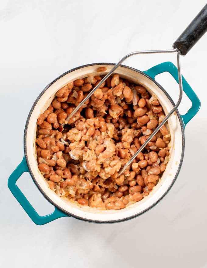 Top view of a cooking pan with the beans being mashed.