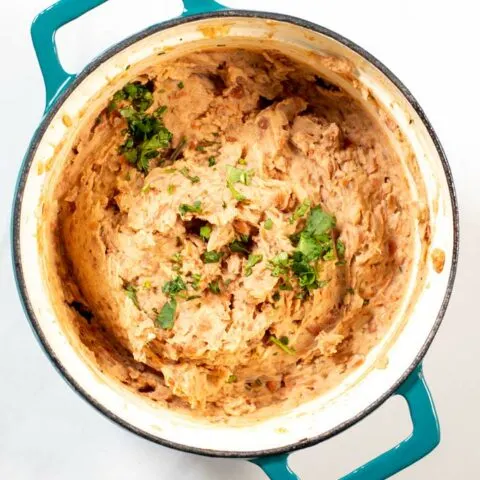 Top view of a pot with refried beans, garnished with fresh herbs.