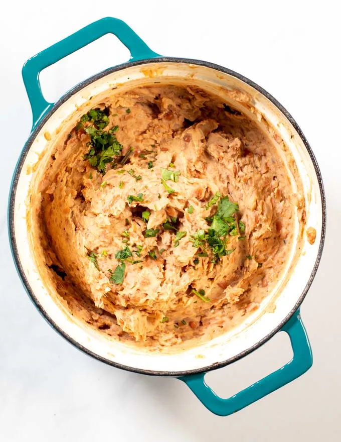 Top view of a pot with refried beans, garnished with fresh herbs.