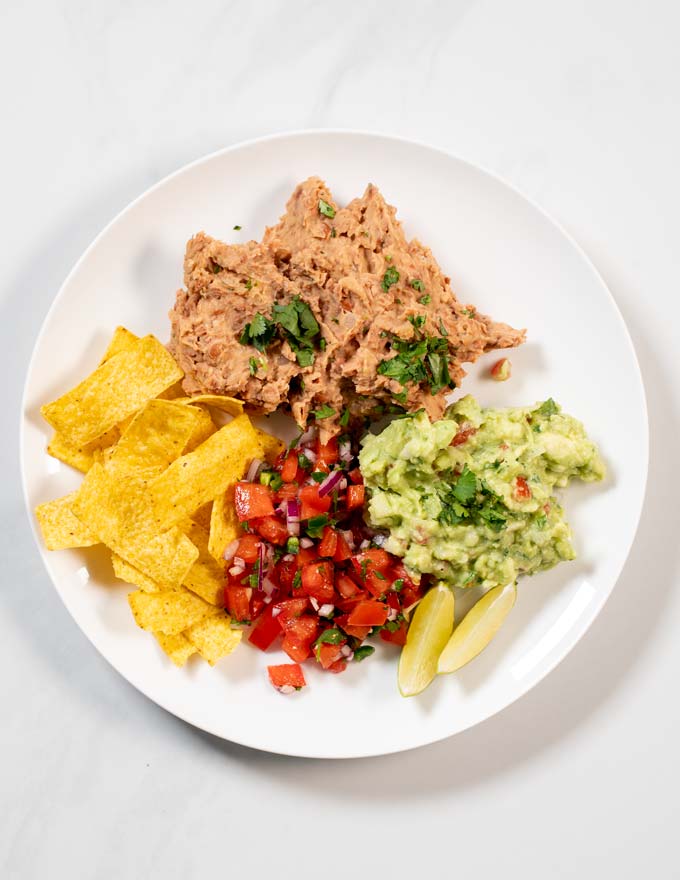 A portion of Refried Beans served with tortilla chips, Pico de Gallo, and avocado.