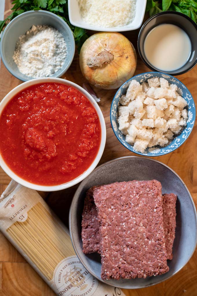 Ingredients needed for making Spaghetti and Meatballs are collected on a wooden board.