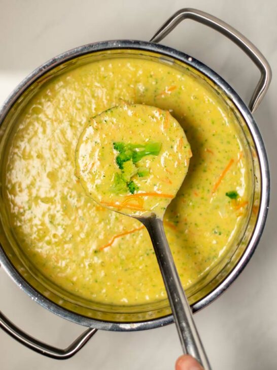 A large spoonful of Broccoli Cheddar Soup is lifted from the pan.