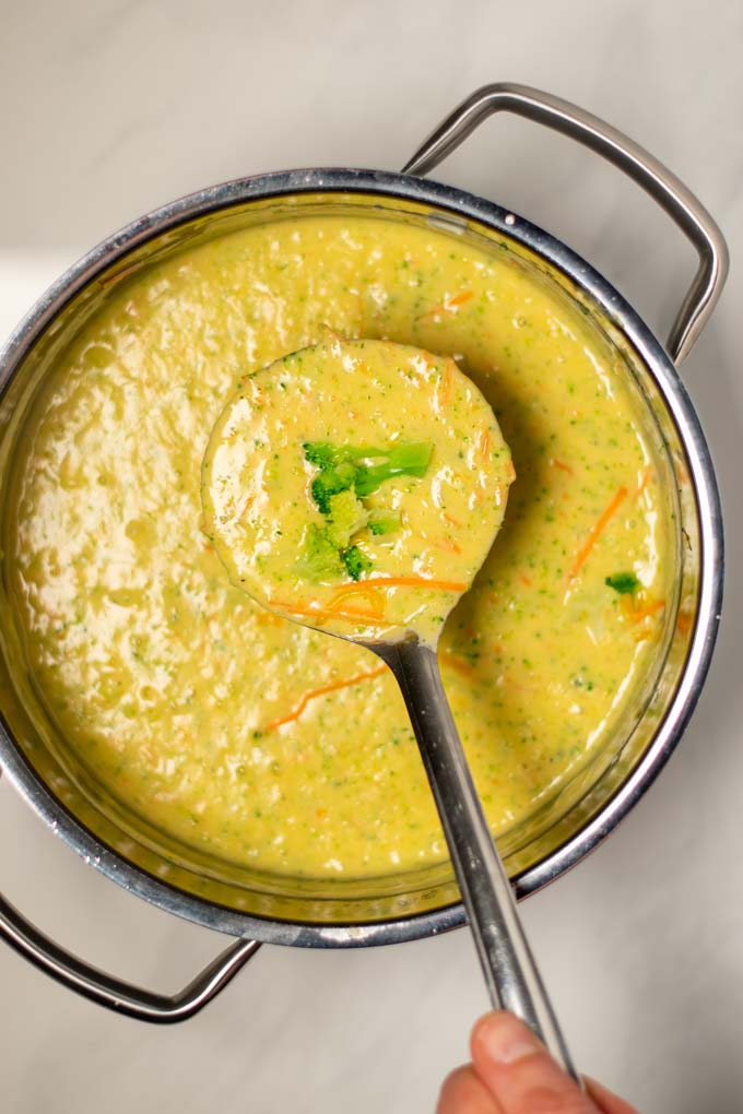 A large spoonful of Broccoli Cheddar Soup is lifted from the pan.