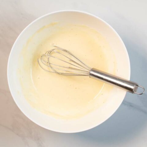 View of a bowl with the mixed Caesar Dressing and a wire whisk.