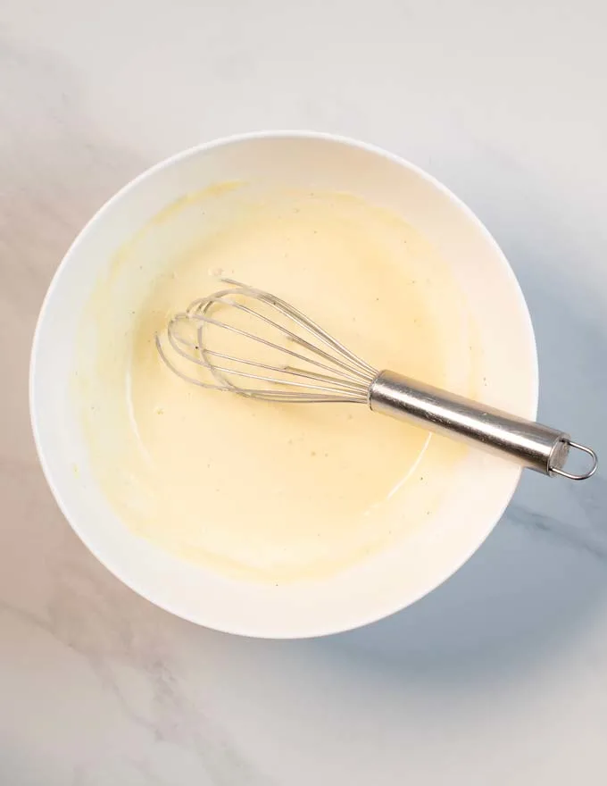 View of a bowl with the mixed Caesar Dressing and a wire whisk.