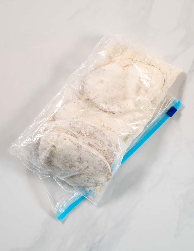 Vegan chicken filets are dredged in flour using a ziplock bag.
