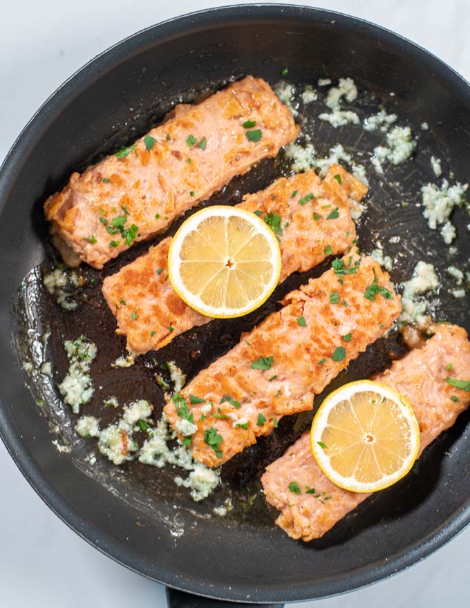 Top view of a pan with Pan Seared Salmon garnished with lemon and herbs.