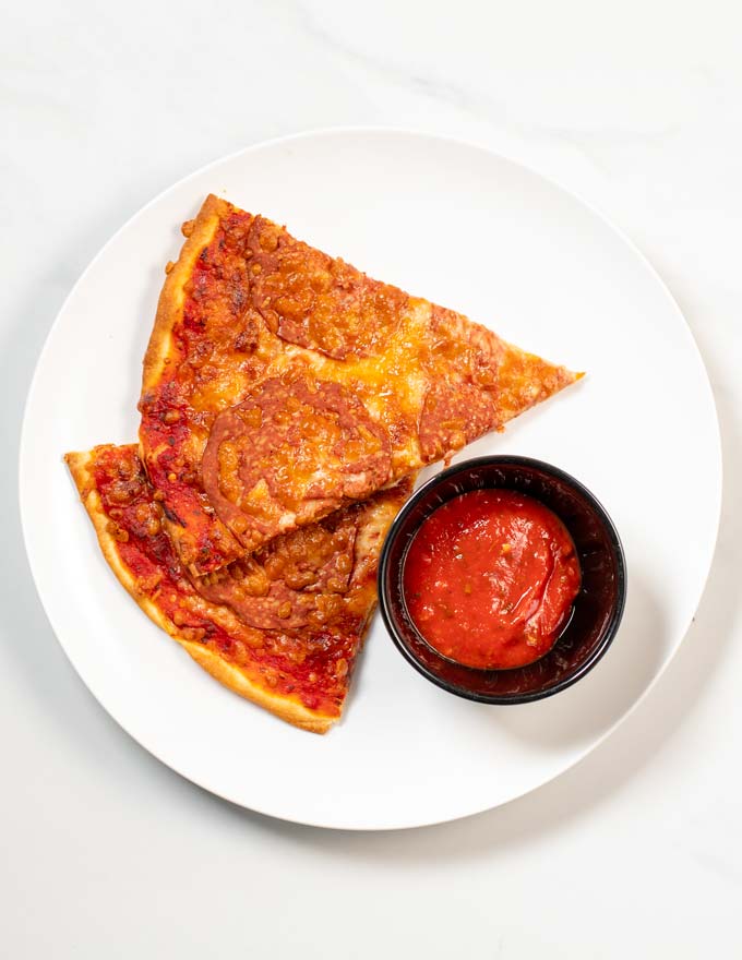 Two slices of pizza are served with extra Pizza Sauce as dipping sauce.