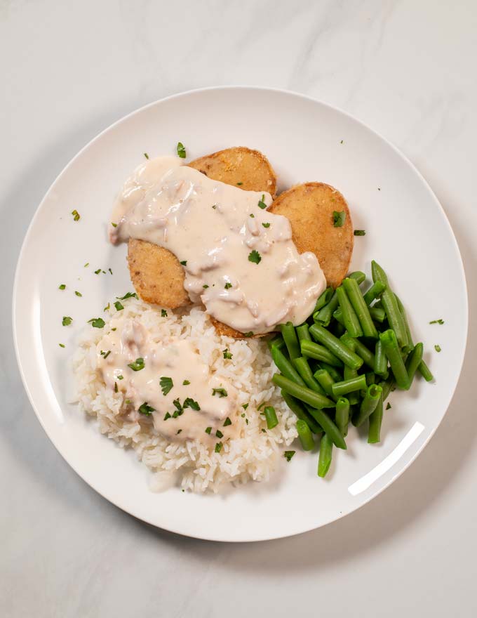 Portion of Smothered Chicken served with rice and green beans on a plate.