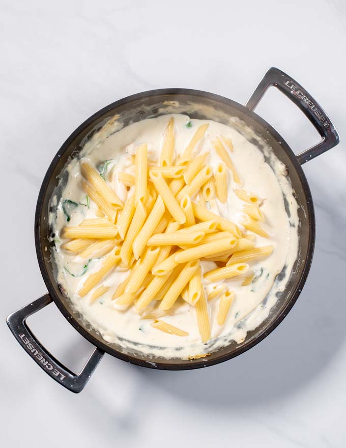 Cooked pasta is added to the creamy sauce in a pan.