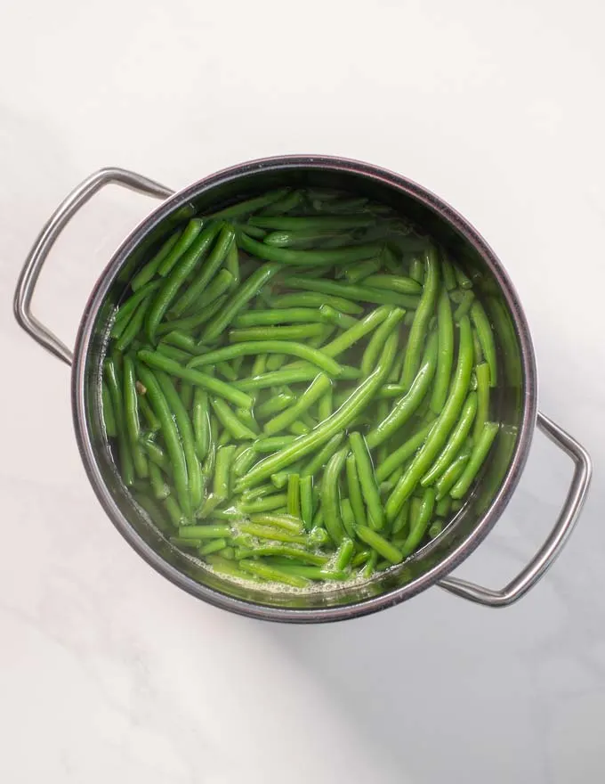 Top view of a large pot in which green beans are boiled.