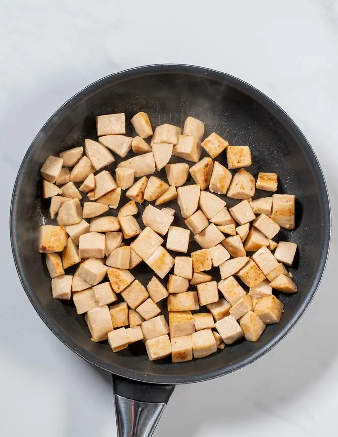 Top view of a pan with vegan chicken cut in cubes being fried.