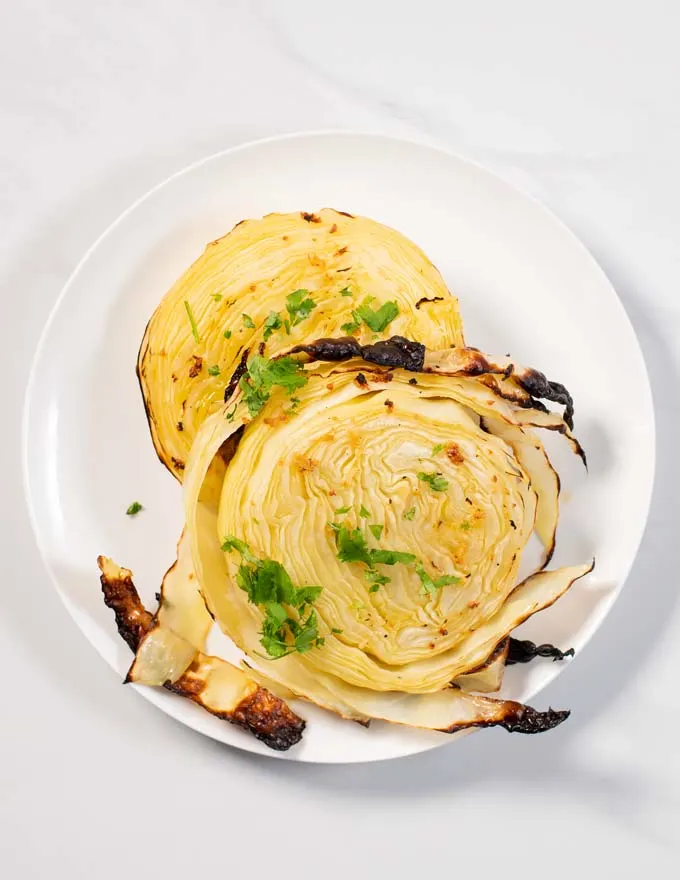 Two Cabbage Steaks are served on a while plate.