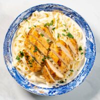 Top view of a serving of Chicken Alfredo, garnished with fresh herbs.