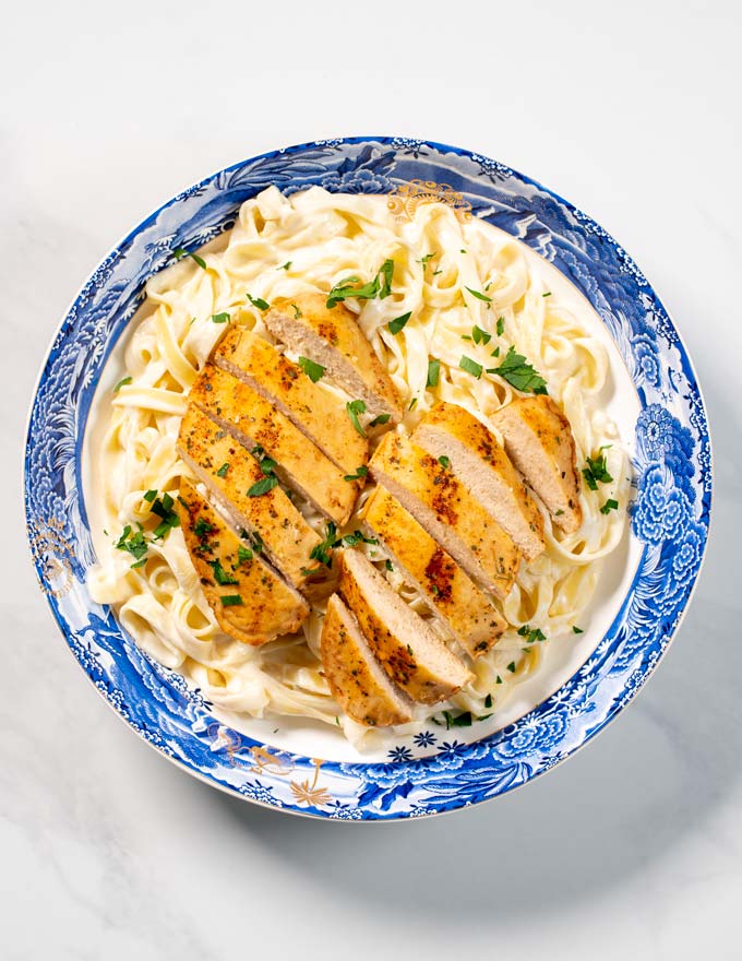 Top view of a serving of Chicken Alfredo, garnished with fresh herbs.
