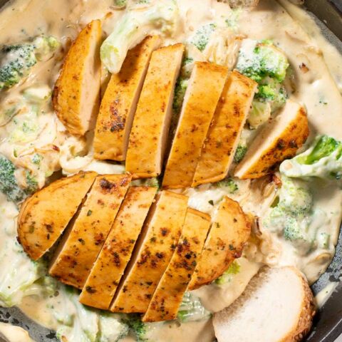 Closeup view of thinly cut chicken filets on to of Broccoli Alfredo Sauce.