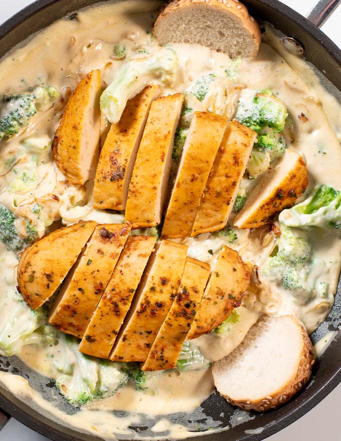 Closeup view of thinly cut chicken filets on to of Broccoli Alfredo Sauce.