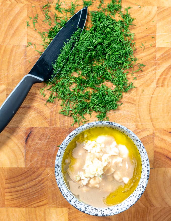 View on a a cutting board with liquid ingredients in a mixing bowl and cut fresh dill.