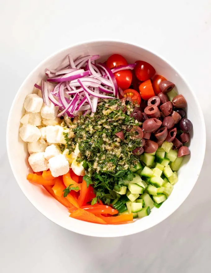 Top view of a large mixing bowl with Greek Salad ingredients and dressing.
