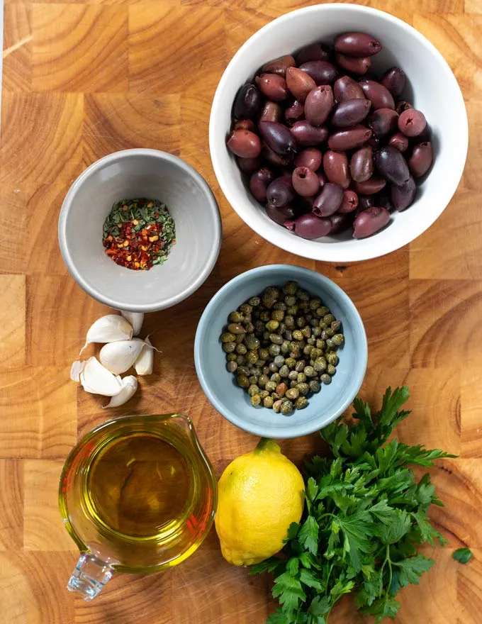 Ingredients needed to make Olive Tapenade on a board,