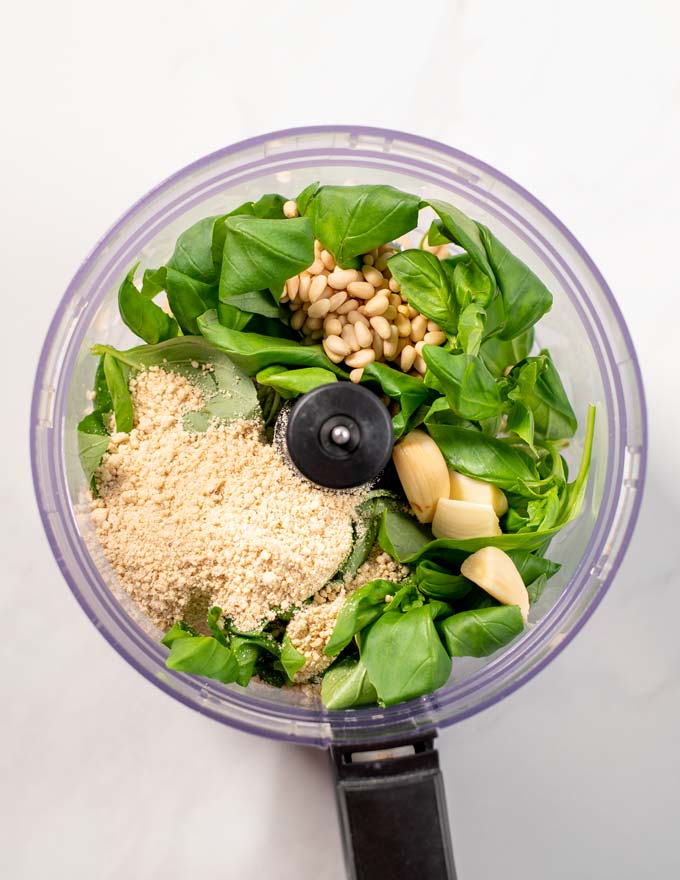 Top view of the mixing bowl of a food processor with the pesto ingredients.