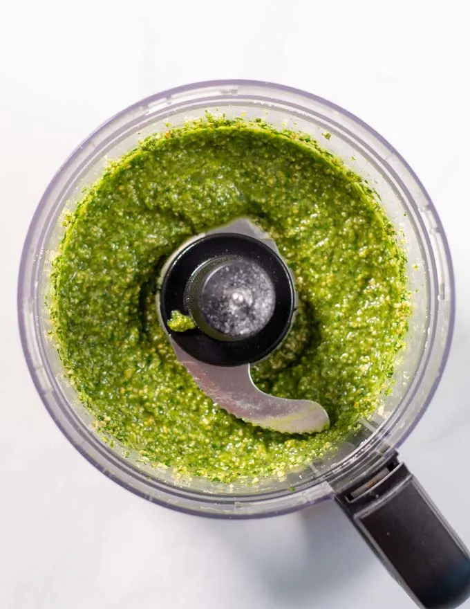 Top view of a bowl of a food processor with the ready green pesto.