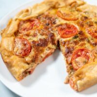 Tomato Pie with a missing piece on a white serving plate.