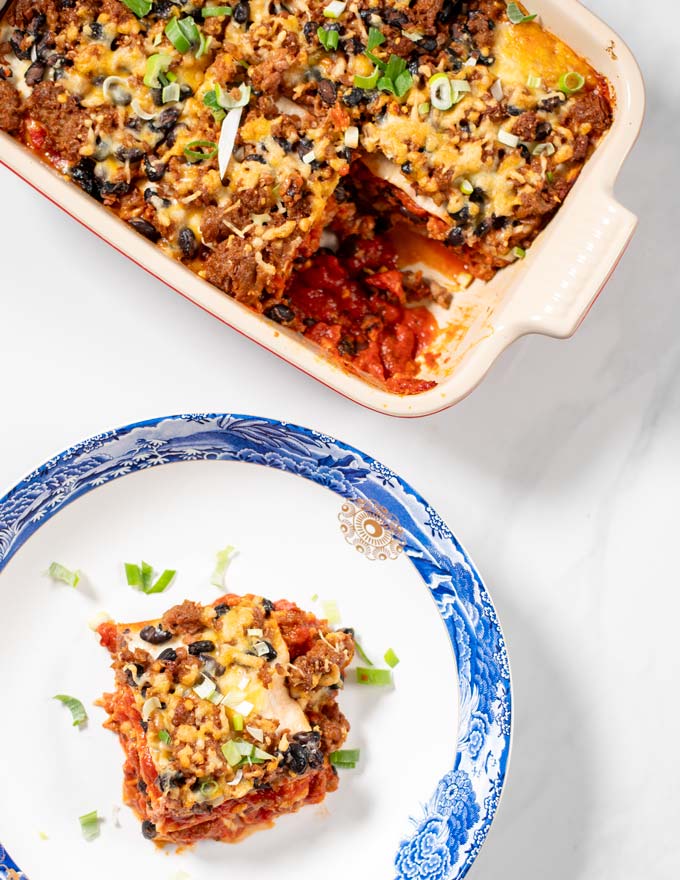 A portion of Enchilada Casserole on a white plate with the casserole dish in the background.