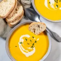 A slice of bread is dunked into Pumpkin Soup.