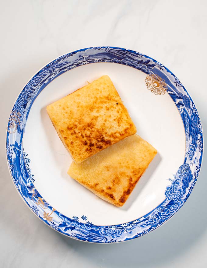 Two pieces of golden brown Saganaki on a serving plate.